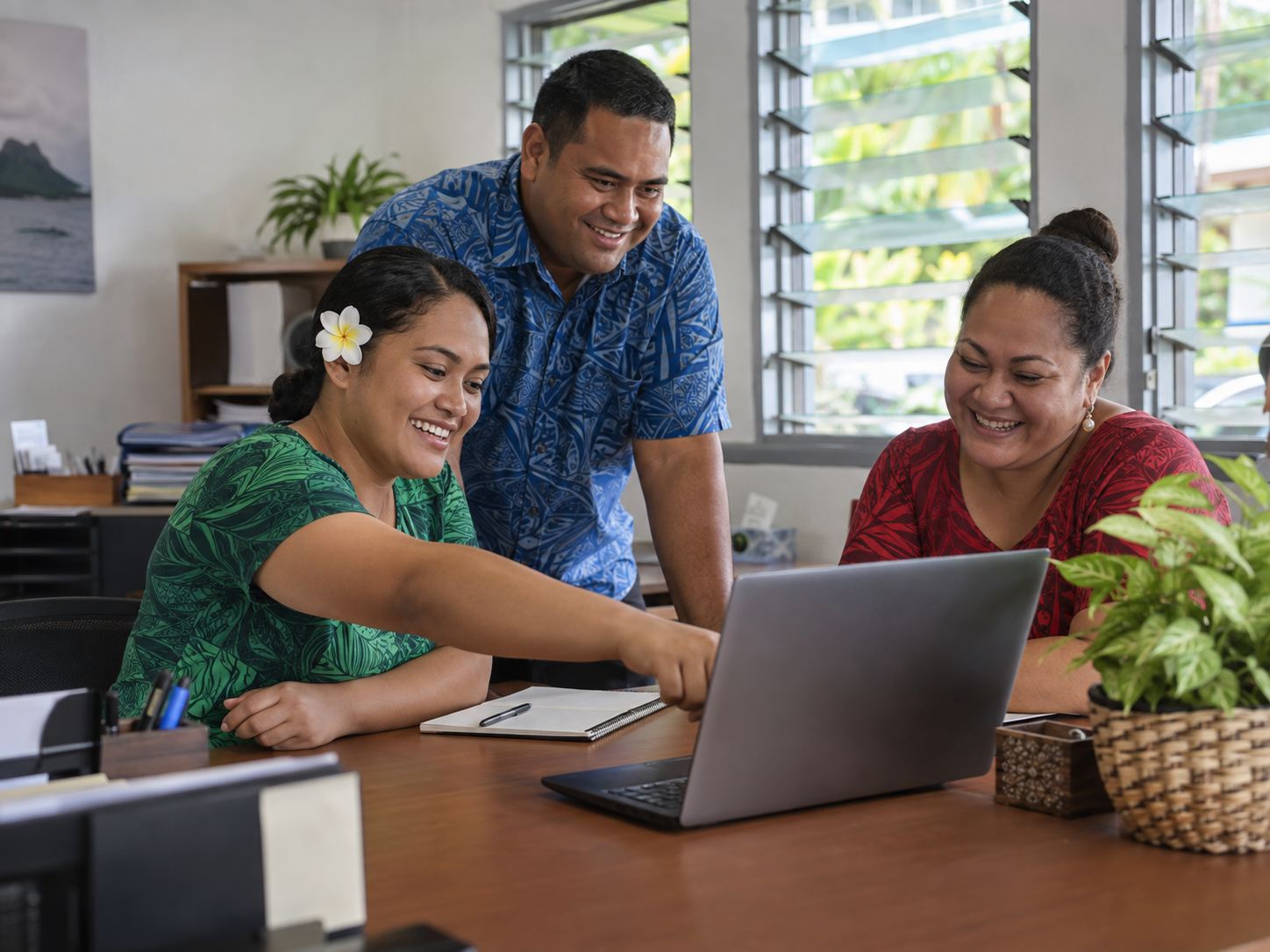 Three office workers in Apia laughing together over a laptop